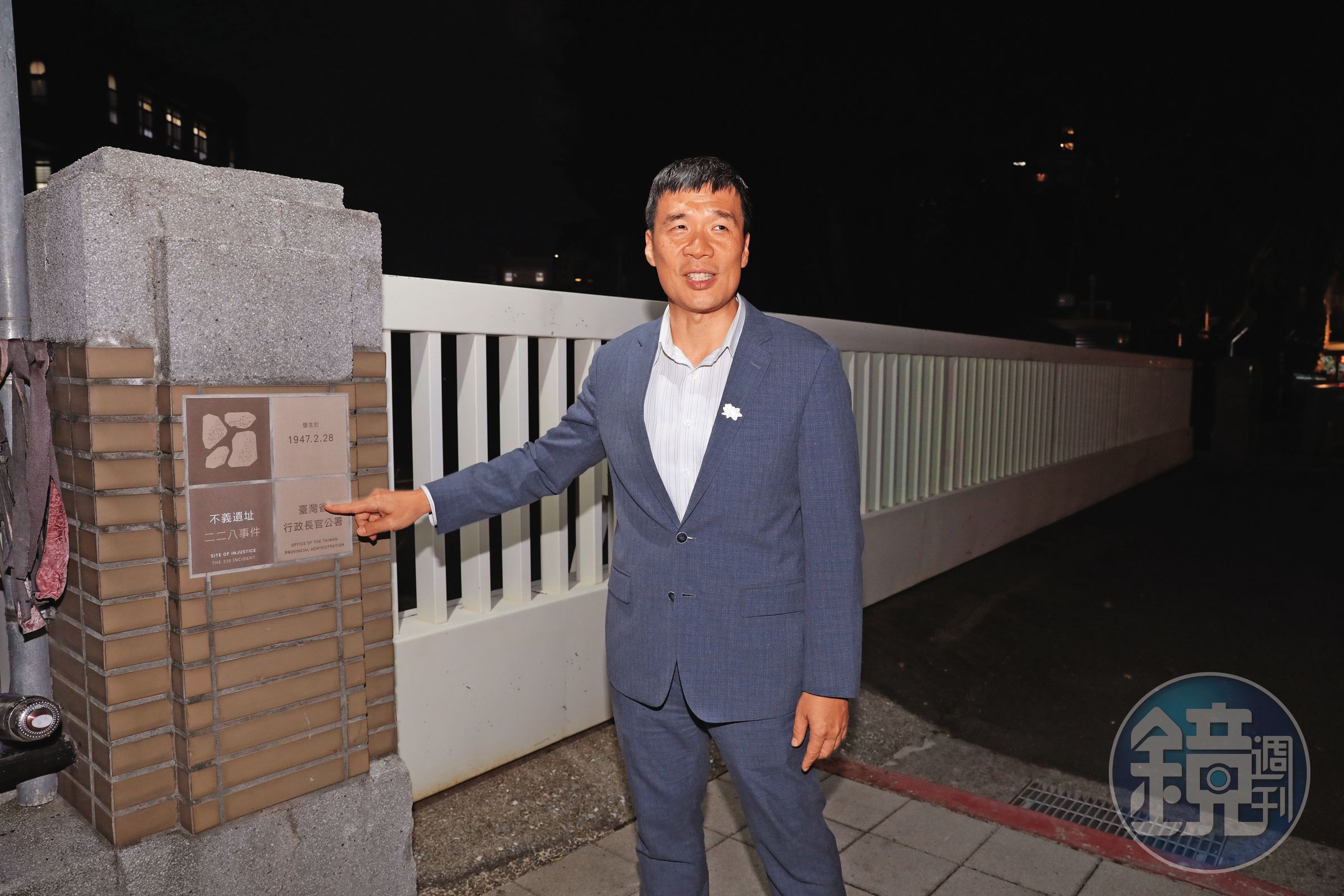 行政院人權及轉型正義處長賴俊兆指著行政院門口的「不義遺址」告示牌，周遭另有標示講述空間與228事件的關聯及目擊者證詞。