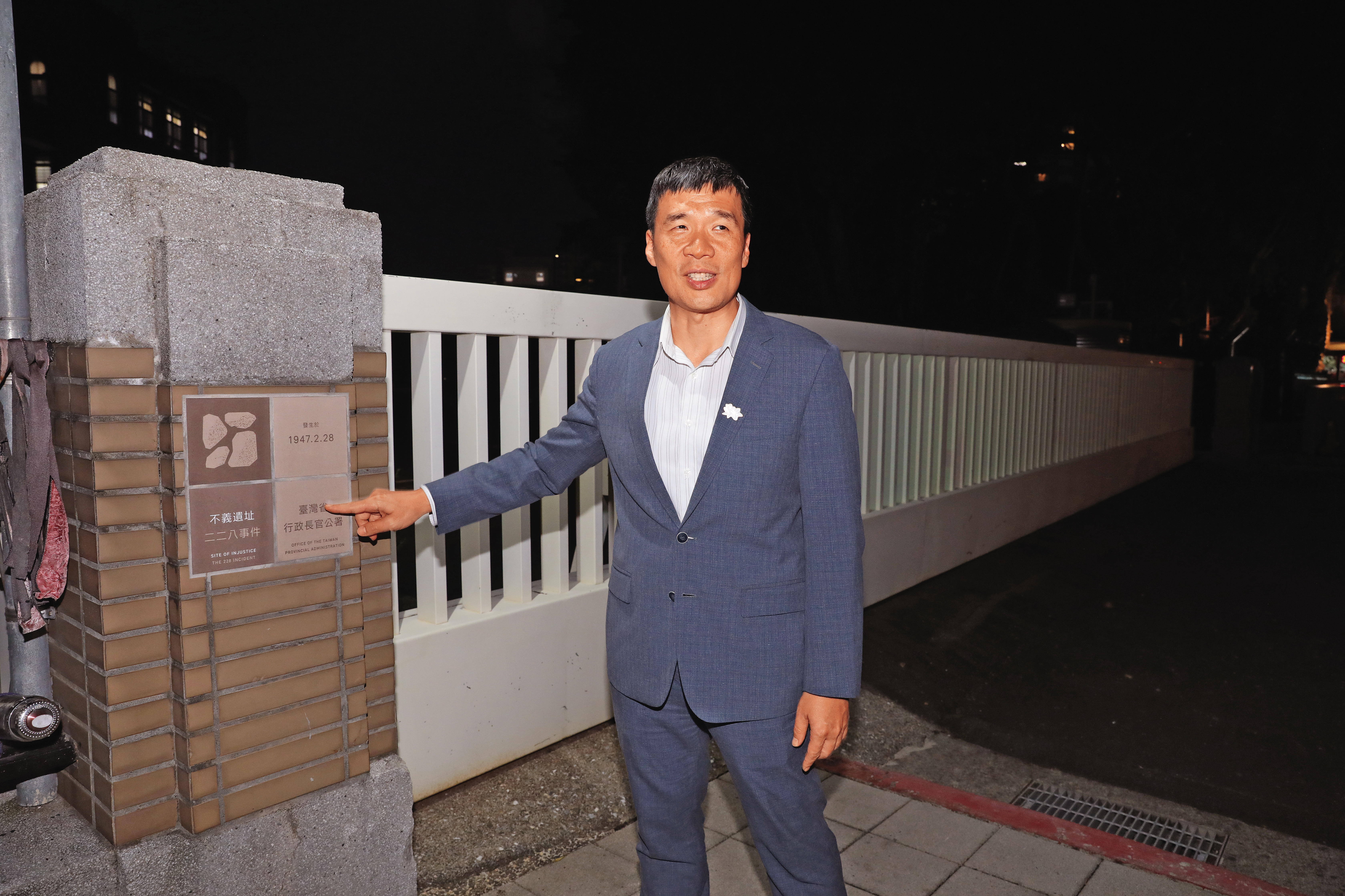 行政院人權及轉型正義處長賴俊兆指著行政院門口的「不義遺址」告示牌，周遭另有標示講述空間與228事件的關聯及目擊者證詞。