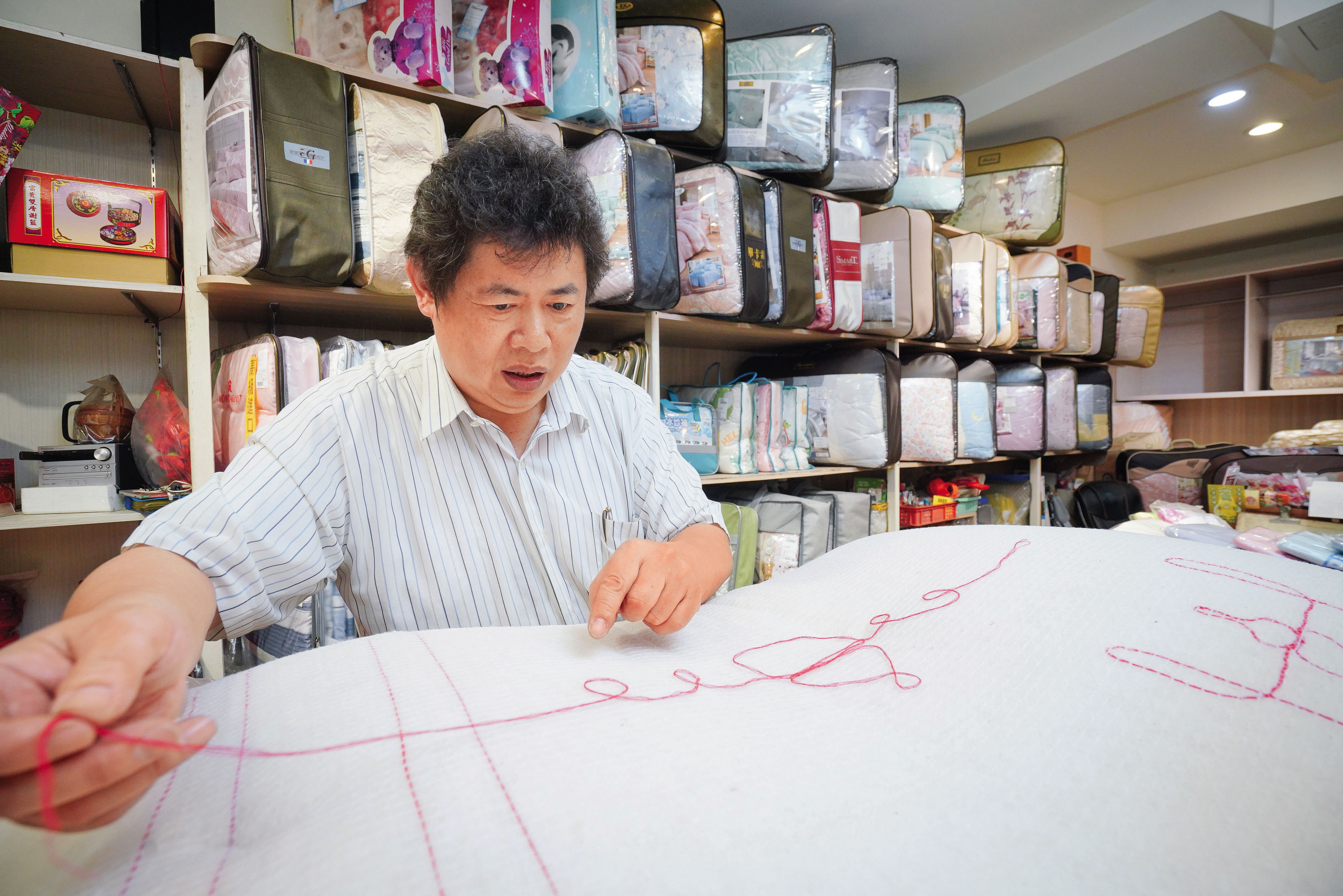 古代手工棉被行普遍沒有店名，師傅以自創商標識別。張寶仁示範祖傳「葫蘆」標誌如何編織。