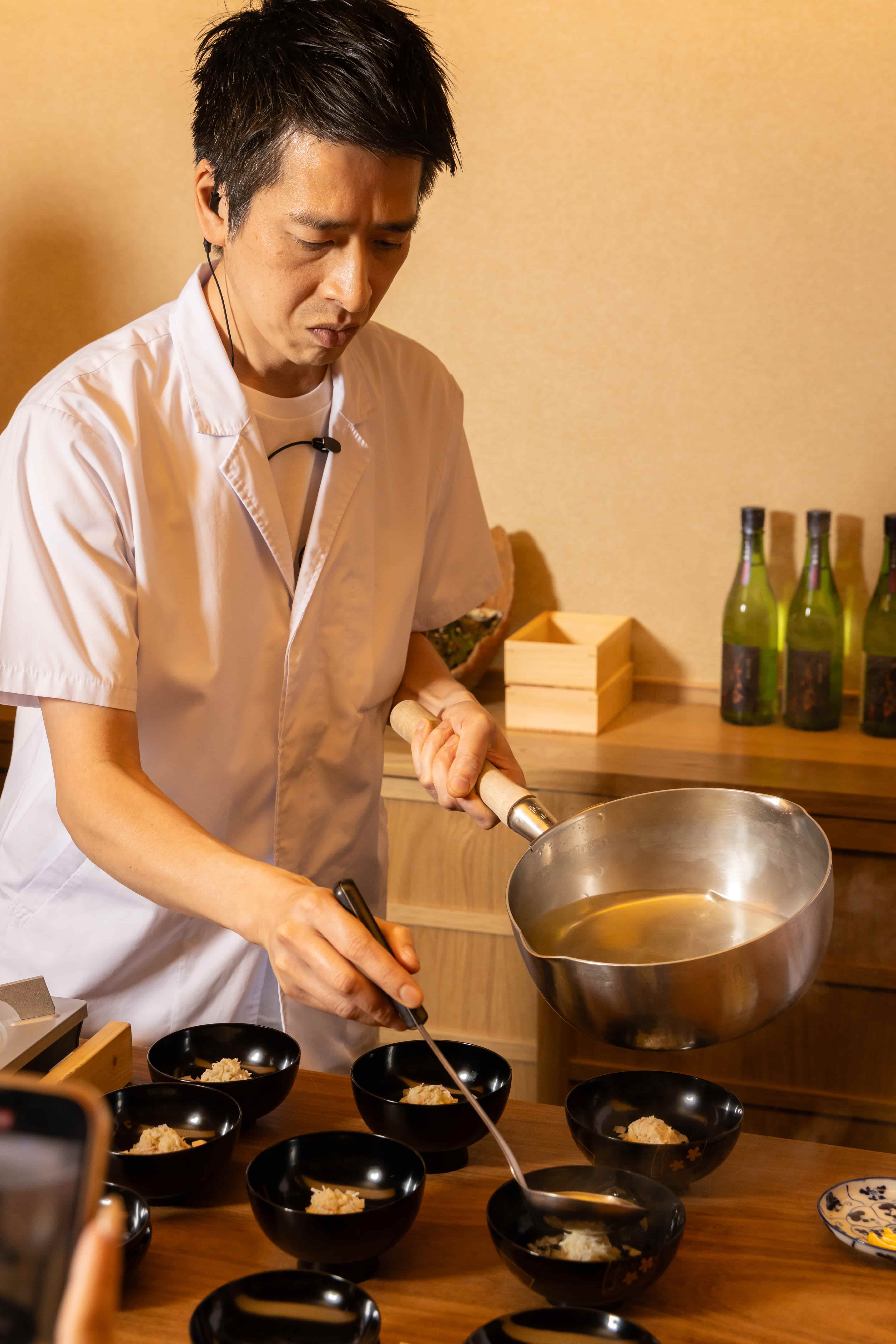 小田建治料理長師在每個碗中放入「松葉蟹真丈」後，緩緩沖入高湯。