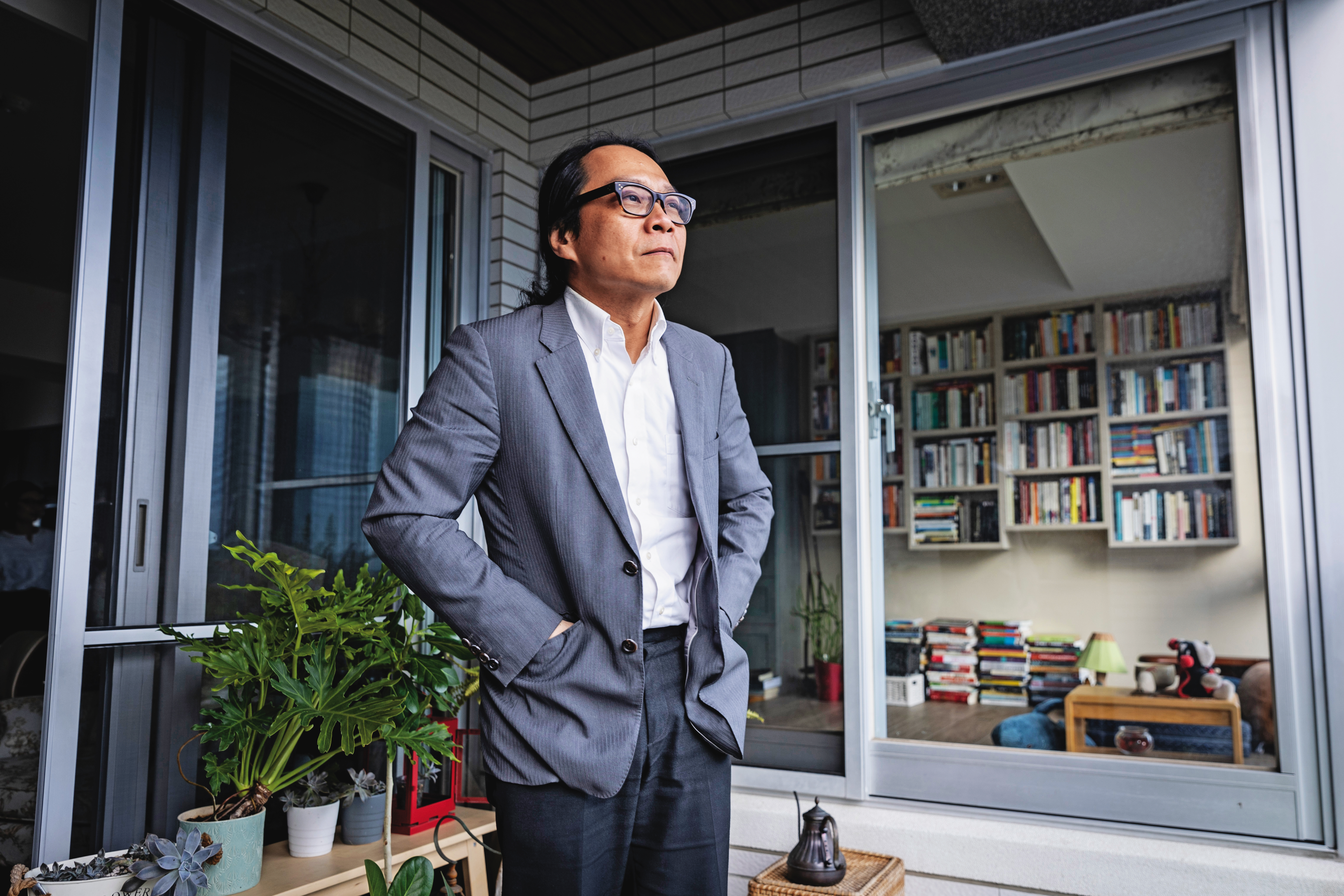今年是葉浩返台後的第18年。圖為葉浩站在自家陽台，窗內是他的部分藏書。