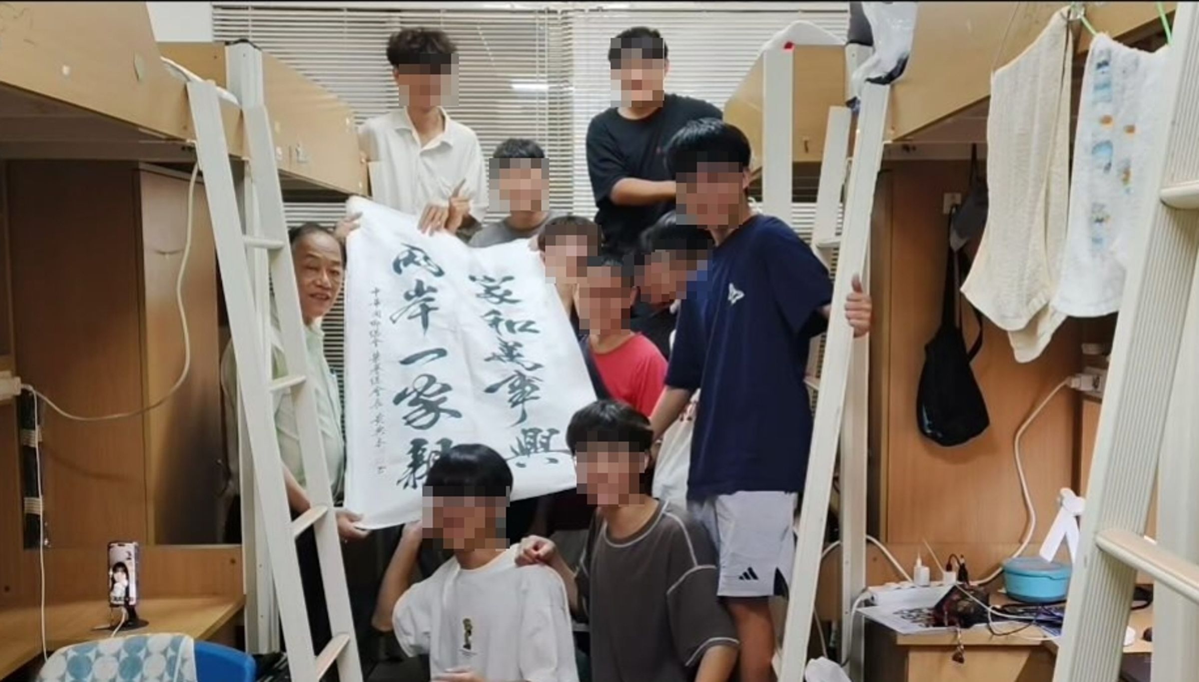 文化大學宿舍大合照中,69歲博士阿伯舉著「兩岸一家親」書法,畫面在網路瘋傳。(翻攝自Threads)