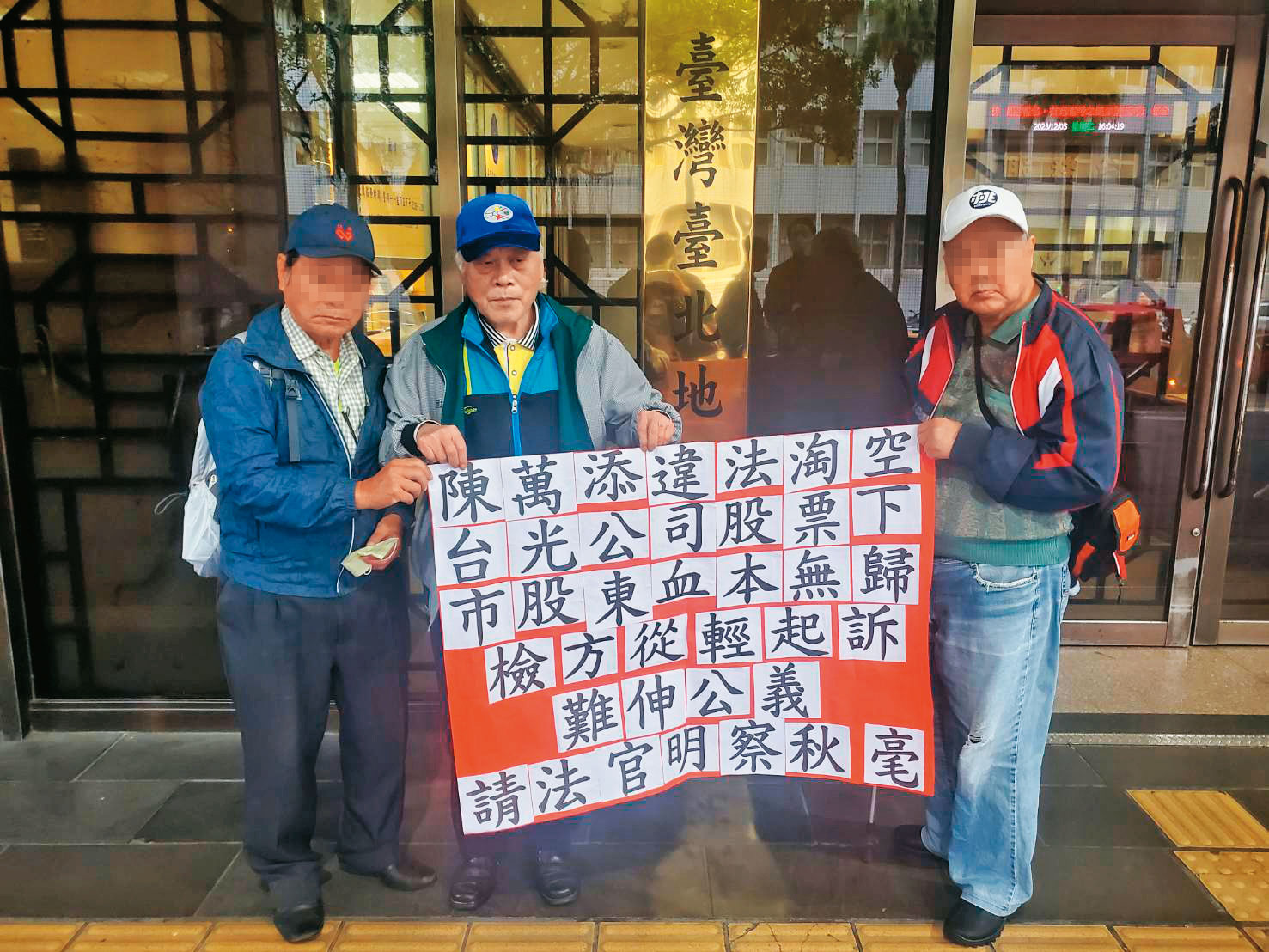 金山財神廟前董事長鄭楠興（中）與受害股東代表在法院外拉布條，籲請法官對陳萬添從重量刑。（讀者提供）