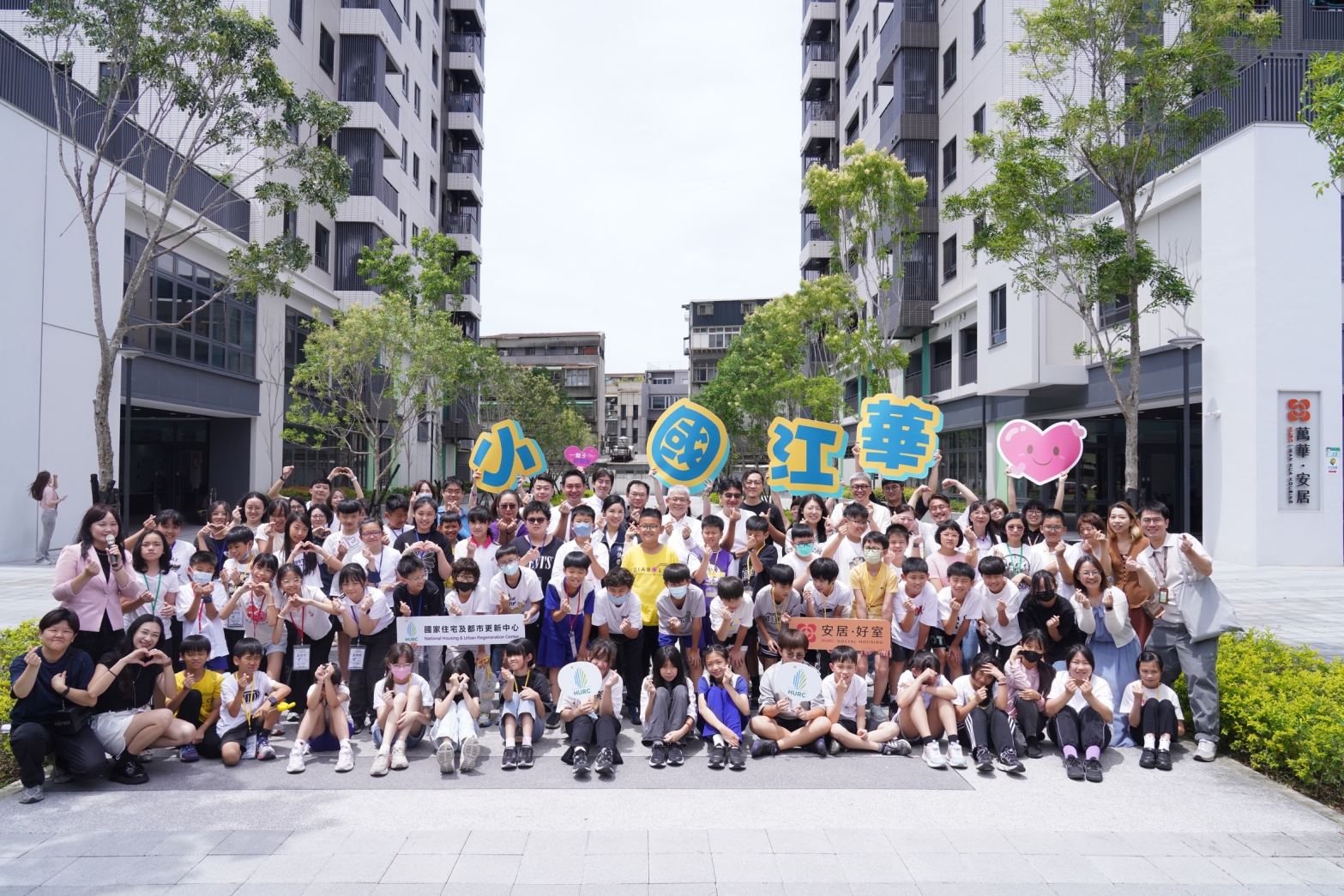 「從華江看天下:尋在地‧探華江‧展風貌—我們華江的故事」成果發表會,出席貴賓與華江國小師生於「萬華安居」社會住宅前合影。(圖/國家住都中心提供)