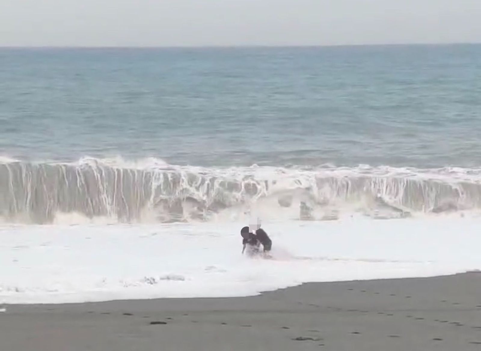 2名黑衣男子在颱風天,還跑到海邊狂奔,甚至有1人被推倒在白浪與沙灘交界處,險些被滾滾海水吞沒。(海巡署提供)