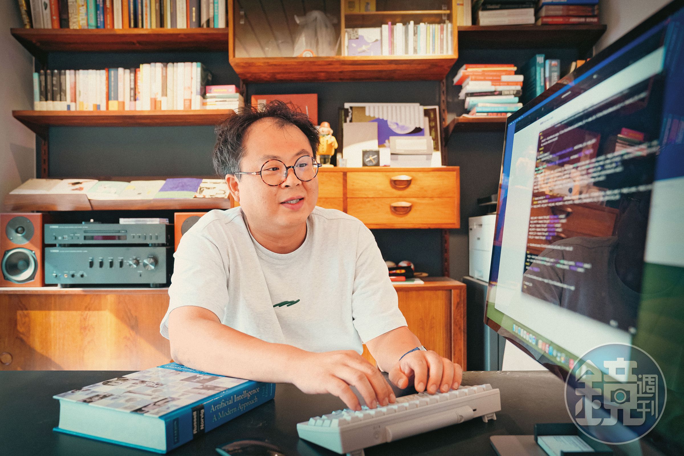 林聖修與我們相約啟明出版社辦公室，辦公桌上放置「以程式設計師理想的鍵位布局」為概念而製作的鍵盤HHKB，手邊原文書是在美念書時，學習人工智慧的課本。