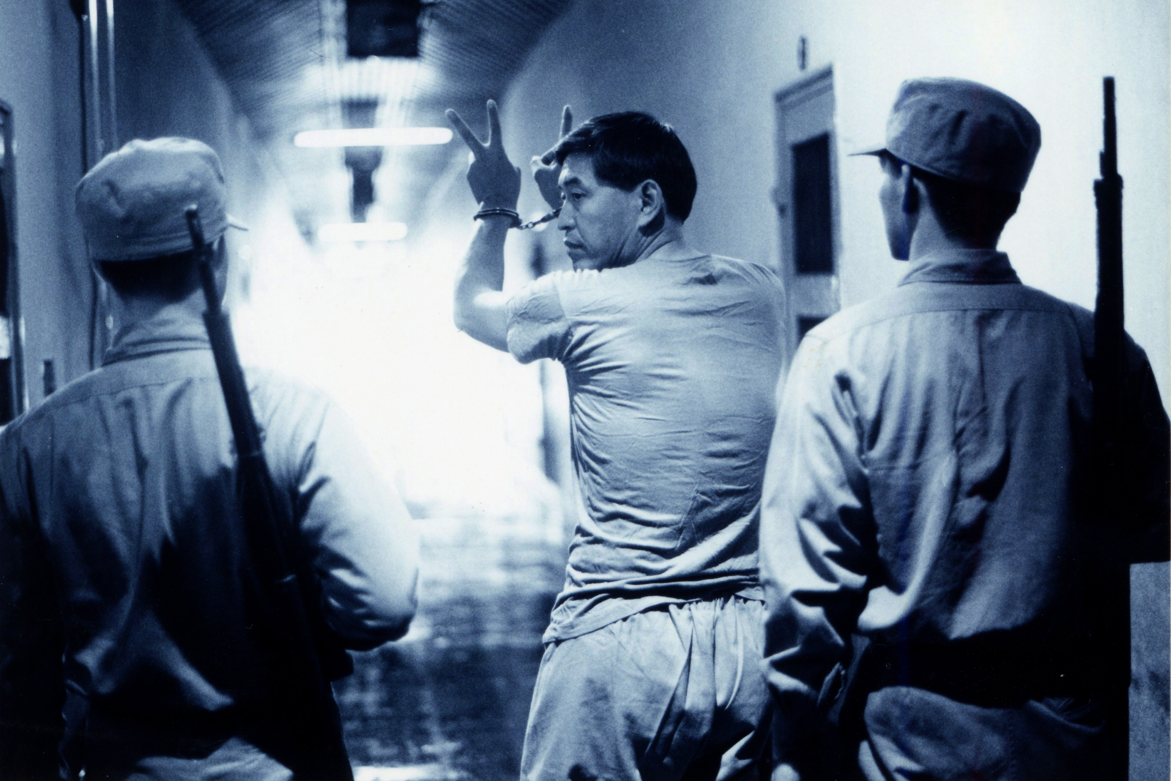 《超級大國民》柯一正（中）飾演的角色在遭槍決前比出數字二一手勢。（國家影視聽中心提供）