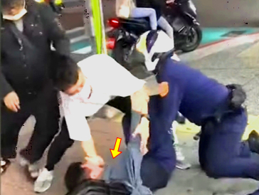 黃先生（箭頭處）被員警推倒在人行道上，一旁的民眾也上前協助員警逮人。（翻攝畫面）