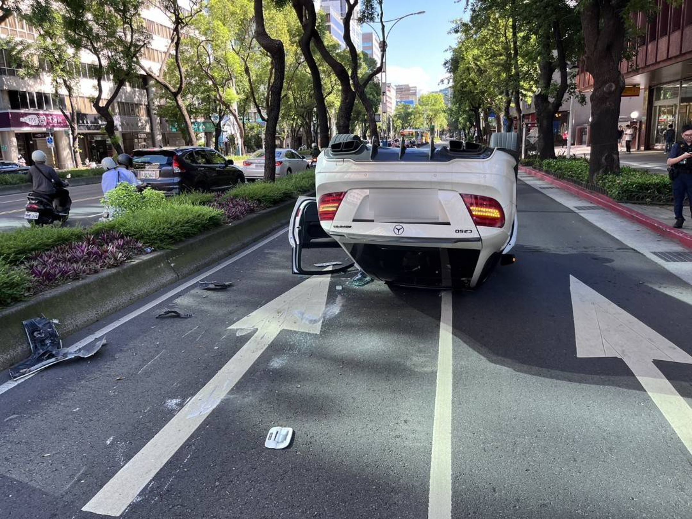 白色賓士轎車因擦撞分隔島導致翻覆,四輪朝天。(翻攝畫面)