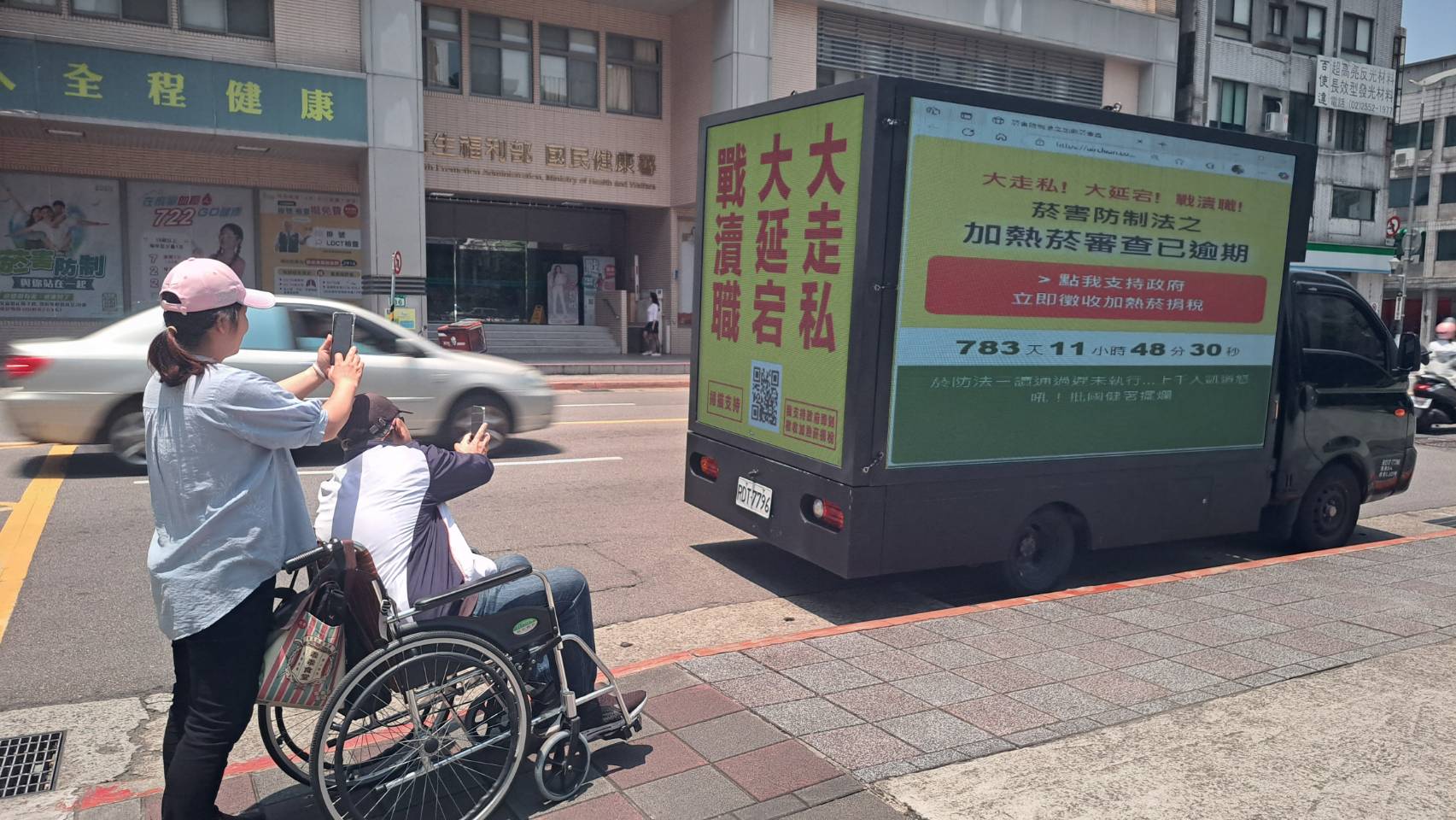 一位輪椅長者在看護協助下前往參與連署掃碼，懇請政府別讓長照資源中斷。（CleanAir大聯盟提供）